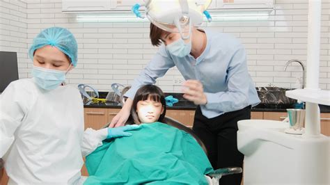 Asian female pediatric dentist checks and examines girl's teeth with