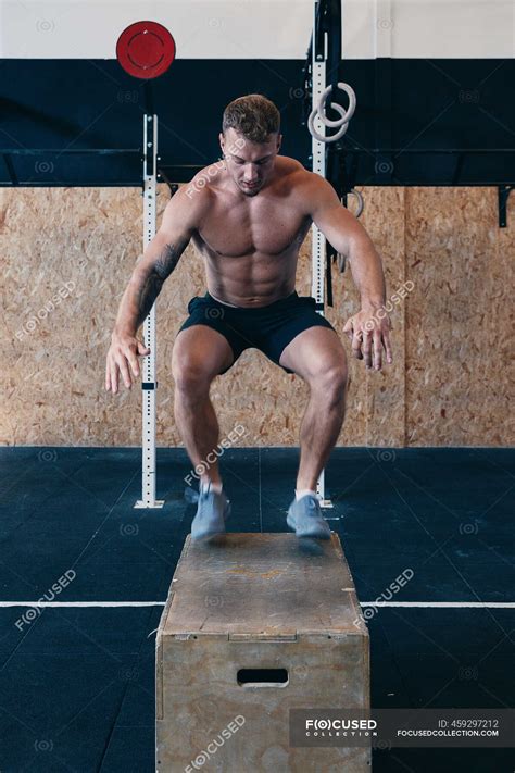 Muscular male athlete with naked torso jumping on wooden box during