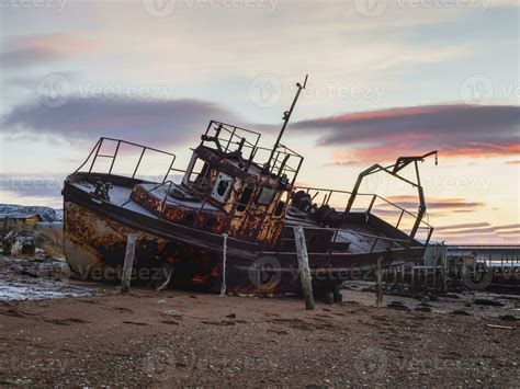 An old rusty fishing boat washed up on a sandy beach in the Barents Sea