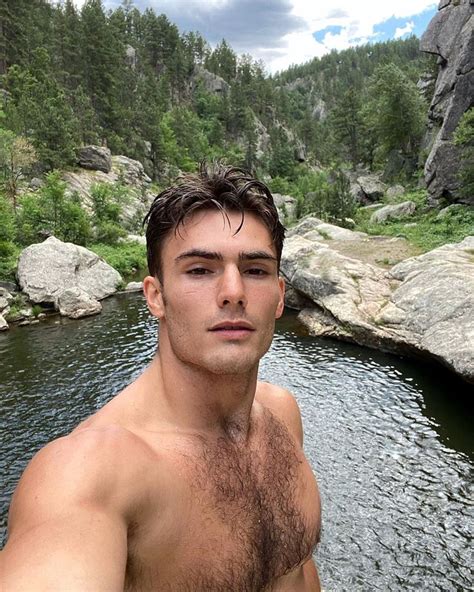a shirtless man standing in front of a body of water with trees and