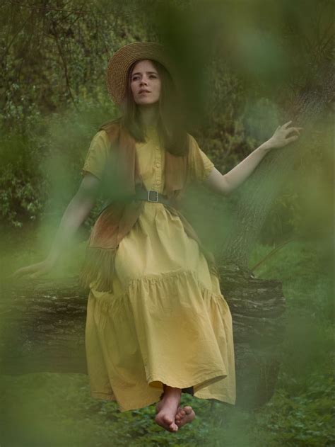 a woman in a yellow dress and straw hat is sitting on a tree stump with ...