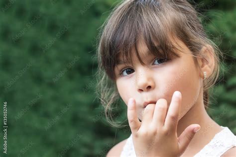 Portrait of brunette little girl licking her fingers outdoors. Girl is