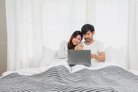 Young happy asian couple using laptop in bed watching movie, romantic