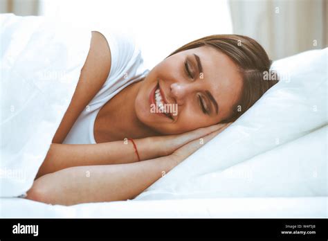 Beautiful young and happy woman sleeping while lying in bed comfortably and blissfully smiling ...