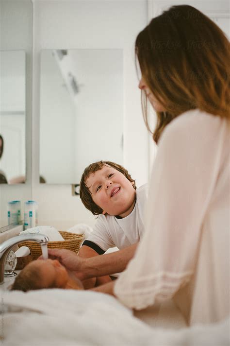 "Son Looking At Mom While She Baths Newborn In Sink" by Stocksy