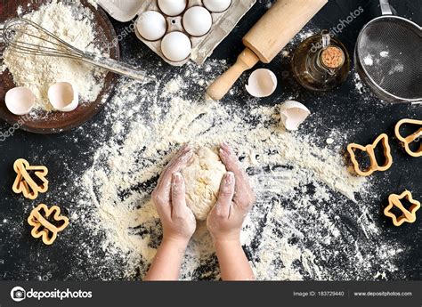 Женские руки месят тесто на столе с мукой, яйцами и ингредиентами. Вид ...