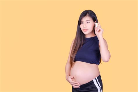 A beautiful pregnant Asian woman touches her belly and uses an ear