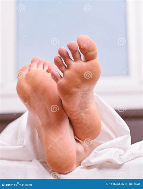 Feet Appear Out of Blanket Close Up. Man Sleeping on Bed Under Blanket