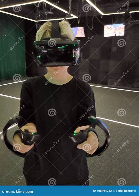 A Teenage Boy with Blond Hair in a VR Headset Standing with Controllers