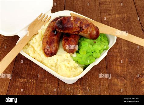 Sausages and mashed potato with mushy peas meal in a take away box on a wooden background Stock ...