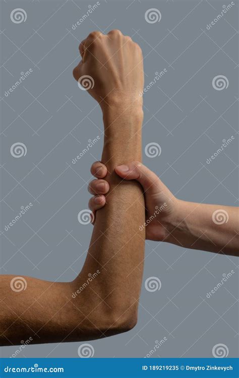 close   light skinned hand clenching dark skinned forearm stock