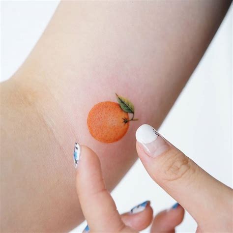 Watercolor orange tattoo on the inner arm.