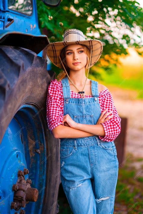 Beautiful blonde cowgirl in straw hat and denim overall standing near