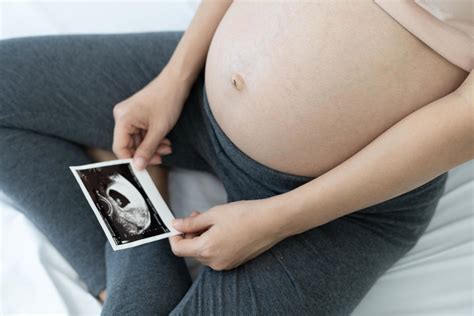 A pregnant woman is looking at an ultrasound photo of fetus. Mother