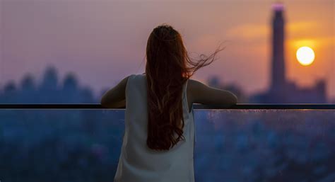 Woman looking and enjoying the sunset view from balcony with the sun