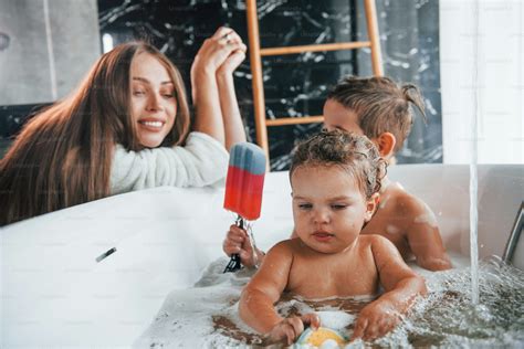 Young mother helps her son and daughter. Two kids washing in the bath