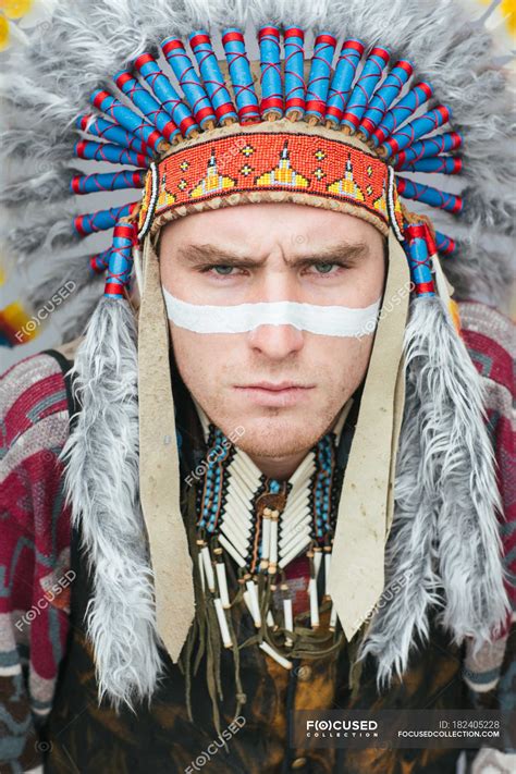 Portrait of man with painted line on face posing in traditional Native
