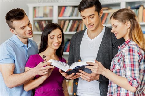 Preparing for their final exams. Four cheerful students reading a book