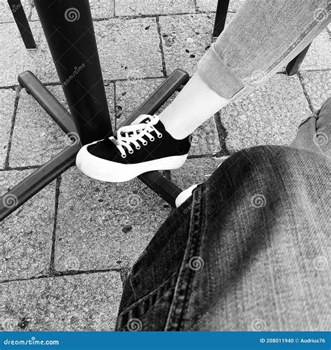 Black and Whit Photo of a Sneaker on the Woman`s Foot Under Street Cafe