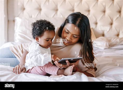 Mixed race Indian black mother with toddler baby girl watching cartoons on tablet. Ethnic ...