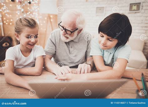 Дед, внук и внучка дома Grandpa и дети используют компьтер-книжку ...
