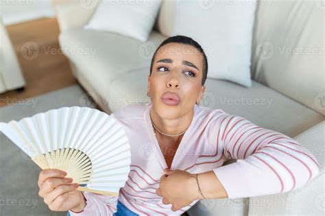 Overheated woman sit on couch at home feel warm waving with hand fan