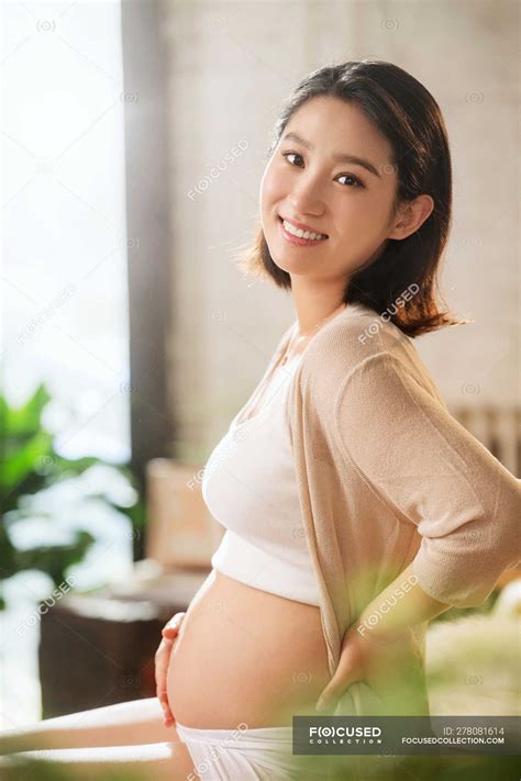 Side view of happy young pregnant asian woman smiling at camera