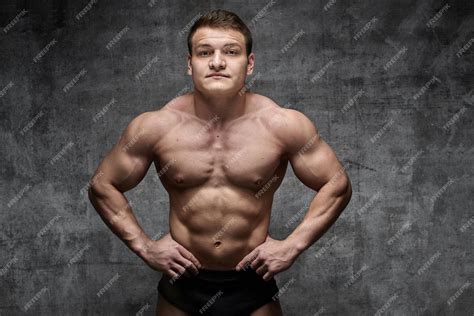 Сексуальный бодибилдер позирует на темном фоне в черных шортах ...