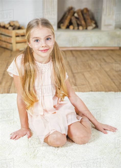 Cute little girl sitting on white carpet and smiling at camera ...