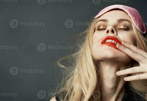 A drunken blonde with a pink sleep mask on her head smears lipstick on