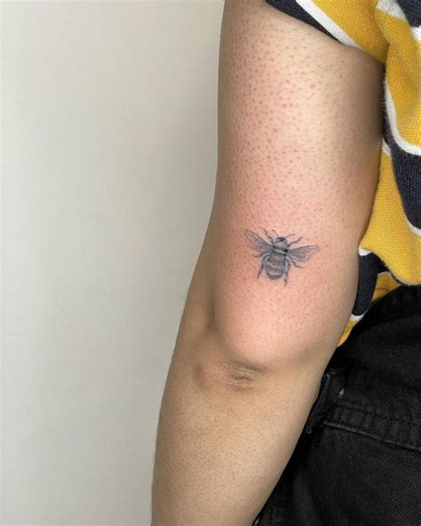 Fine line blue bee tattoo on the tricep.