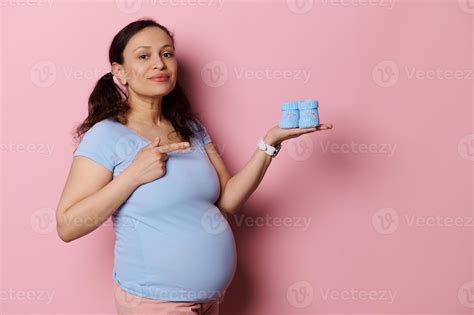 Beautiful Latina pregnant woman pointing finger aside cute blue baby