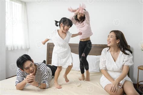 Asian Parents with two little daughters jumping on the bed in bedroom
